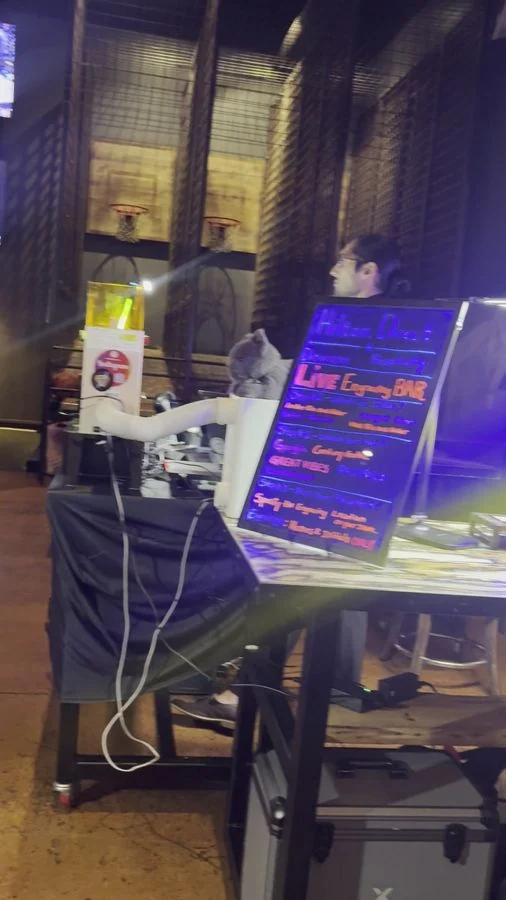 Live Engraving Bar menu sign glowing at the LaserLux Lab booth with the laser operator behind the table
